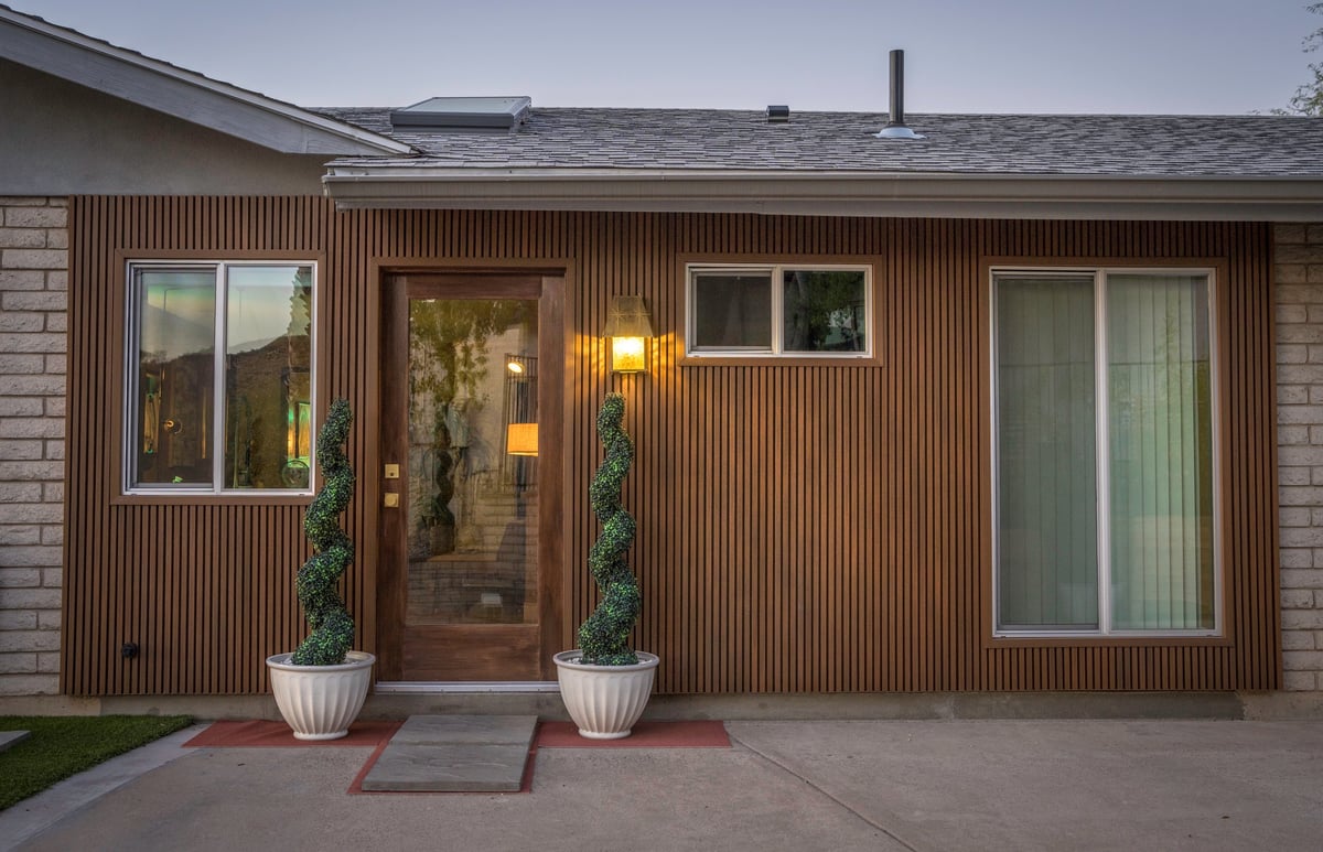 Mid-century home with wood paneling, large windows, and sculpted trees