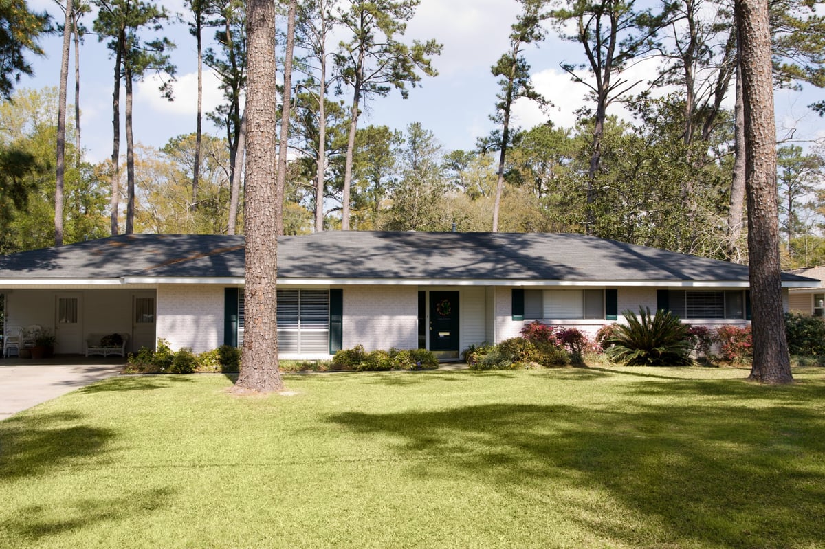 Single-story traditional home surrounded by tall trees and well-manicured lawn