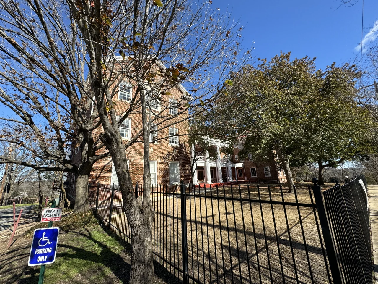 Kirby Hall School behind trees and an iron fence on West 29th Street, north of UT Austin.