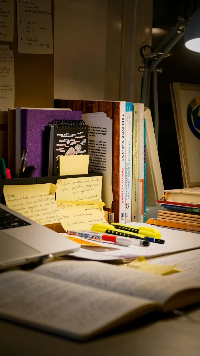 A desk with research books, handwritten notes and a laptop. Illustrative photography, not a local listing.