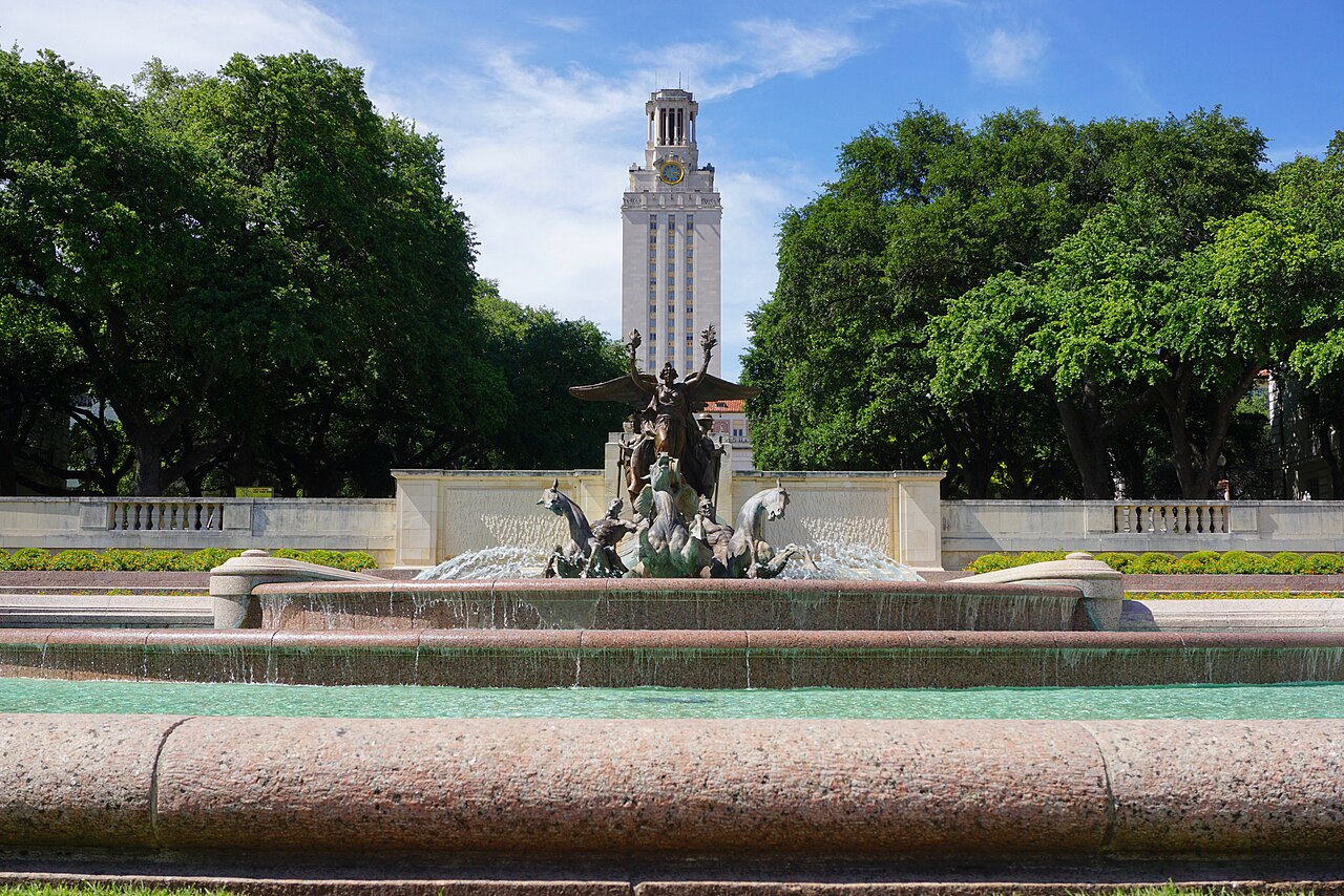 Frog Fountain at Texas Christian University in Fort Worth, Texas — iconic three-tiered bronze fountain with 'TEXAS CHRISTIAN UNIVERSITY' engraved on the limestone base, set against a bright blue sky and modern campus buildings. Independent campus housing information for TCU.